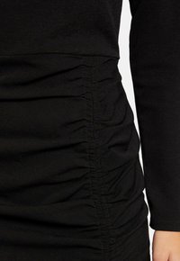 Vestido negro con un diseño ajustado y textura fruncida en un lado, mangas largas y material suave.