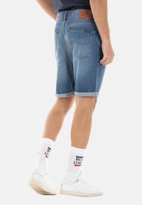 Shorts en denim de couleur bleu clair, avec un ourlet replié et des poches arrière. Portés avec des chaussettes blanches et des baskets, mettant en avant un style décontracté.