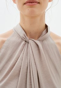 Helles taupefarbenes Halftertop mit einem gerafften Design, bestehend aus weichem, strukturiertem Stoff und einem geknoteten Detail am Ausschnitt.