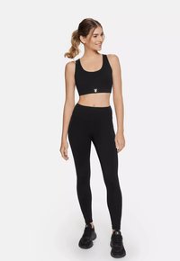 Black sports bra with a rounded neckline, paired with high-waisted black leggings. Smooth fabric, minimal logos, and athletic shoes.