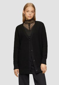 Zwarte gebreide cardigan met V-hals, oversized pasvorm, knopen aan de voorkant en geribde manchetten. Gstyled over een top met ingewikkelde kantdetails.