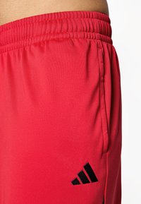 Røde sportsshorts lavet af glat stof med elastisk talje og sort logo på den nederste side. Har sidelommer og en afslappet pasform.