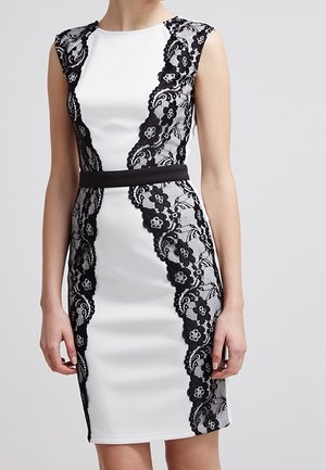 White sleeveless dress with black floral lace panels and a black waistband, fitted silhouette.