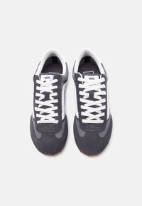 Paire de baskets Vans gris foncé et blanc avec des lacets blancs, vue de dessus sur un fond gris clair uni.