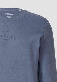 Modrá mikina s okrúhlym výstrihom so zvýšeným logom "s.Oliver" a detailným prešívaním pod golierom, zobrazená z oblasti hornej časti trupu.