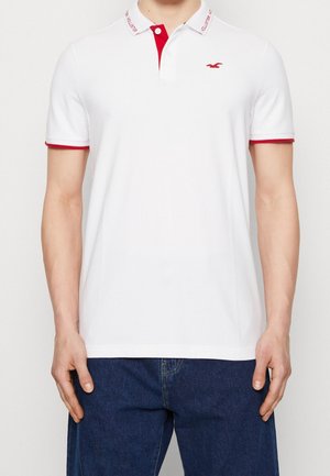 Polo shirt blanc avec des accents rouges sur le col et les manches. Présente un petit logo sur la poitrine, fabriqué en coton doux.