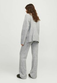 Szary, oversize sweter dzianinowy z prążkowanym wykończeniem, w komplecie z dopasowanymi szarymi spodniami w szerokim kroju. Materiał ma miękką, teksturowaną powierzchnię.