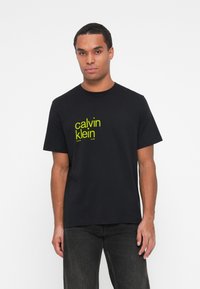 Melnas kokvilnas t-krekls ar neona dzeltenu 'calvin klein' logotipa apdruku priekšpusē. Īsās piedurknes un apaļa kakla izdoma.