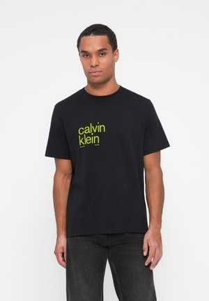 Crna pamučna majica s neonsko žutim printom 'calvin klein' loga sprijeda. Kratki rukavi i okrugli izrez.