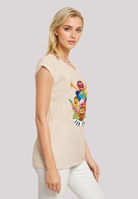 Beige short-sleeve t-shirt featuring a colorful graphic of cartoon characters with musical elements, paired with white pants.