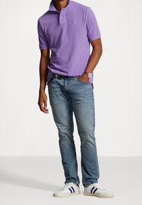 Violetti puuvillapolo paita, jossa on kaulus, yhdistettynä vaaleansiniin farkkuihin ja valkoisiin tennareihin, joissa on tumma raidat. Hopeinen kello mainittu.