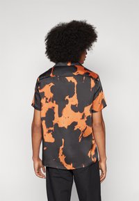 Kortebloeshemd van satijnmateriaal met een abstracte oranje en zwarte patroon, voorzien van een spreidkraag en een comfortabele pasvorm.