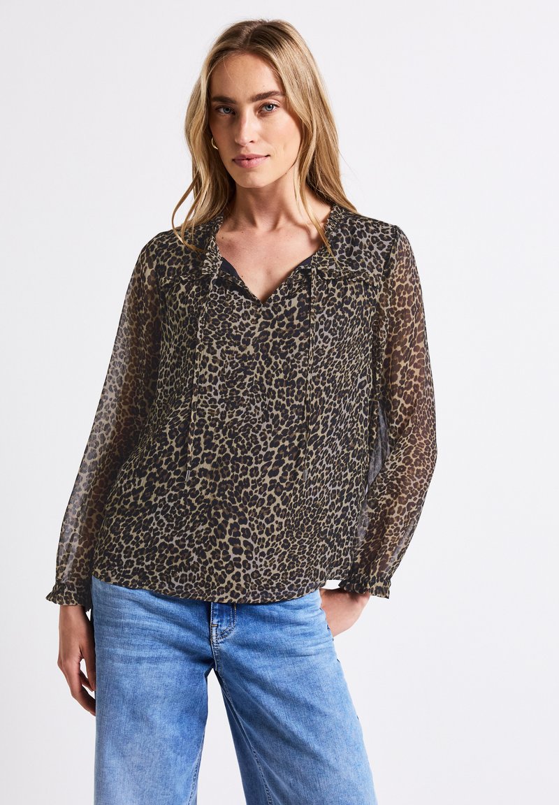 Blusa trasparente a maniche lunghe con stampa leopardata, caratterizzata da una scollatura a V, dettagli plissettati e polsini arricciati. Abbinata a jeans azzurri.