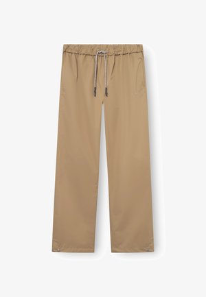 Pantalons imperméables beiges avec une taille élastique et un cordon de serrage réglable. Comprend deux poches latérales et un design décontracté.