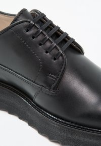 Chaussure montante noire en cuir avec semelle épaisse texturée et coutures détaillées sur la partie supérieure.