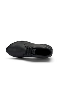 Sneaker in pelle nera con lacci visto dall'alto, che mostra la punta arrotondata, il colletto imbottito e il bordo della suola testurizzata su sfondo bianco.