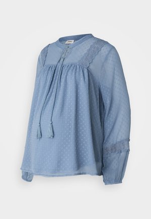 Svijetloplava bluzica od prozirnog materijala s teksturiranim točkicama. Ima okrugli izrez, spušteni struk i čvorove s resicama. Čipkasti detalji na ramenima.