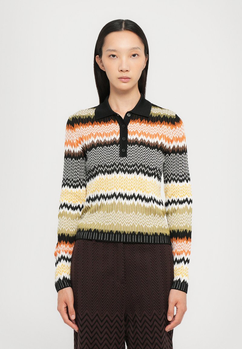 Maglione lavorato a maglia con motivo a zigzag in strisce arancioni, nere, bianche, verdi e gialle. Collo e polsini neri con chiusura a bottone.
