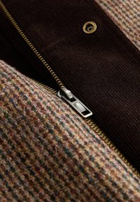 Brown corduroy and textured fabric with a multi-colored pattern. Features a metal zipper and a bronze eyelet detail.