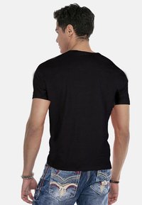 Schwarzes Baumwoll-T-Shirt mit Rundhalsausschnitt, kurzen Ärmeln und normaler Passform, von hinten gegen einen einfarbigen Hintergrund präsentiert.
