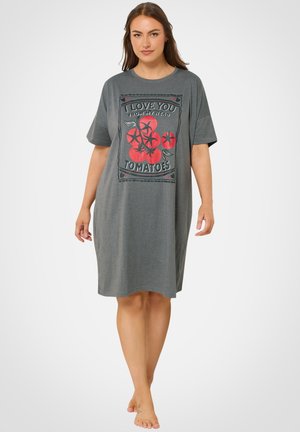 Frau steht barfuß, trägt ein weites graues Kleid mit einer Illustration roter Tomaten und dem Text „Ich liebe dich von meinen Kopf-Tomaten“.
