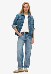 Leren denimjack in lichtblauw met een klassiek ontwerp, gecombineerd met een witte t-shirt en lichtblauwe rechte jeans, afgewerkt met tan sneakers.