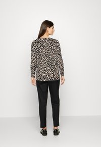 Sweater com padrão de leopardo, mangas longas, decote redondo e textura suave. Combinado com calças pretas e calçado preto.