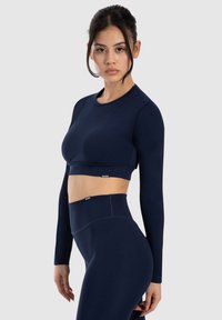 Completo composto da un top cropped a maniche lunghe e leggings a vita alta di colore navy. Tessuto liscio e stretch con cuciture piatte e etichetta del marchio sulla vita.