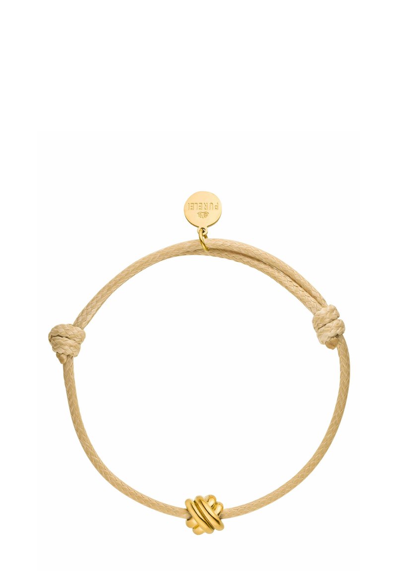 Knot-Armband aus einem beigen geflochtenen Band, verziert mit einem Knoten aus goldfarbenem Metall und einem runden Anhänger. Sanfte Textur mit minimalistischer Gestaltung.