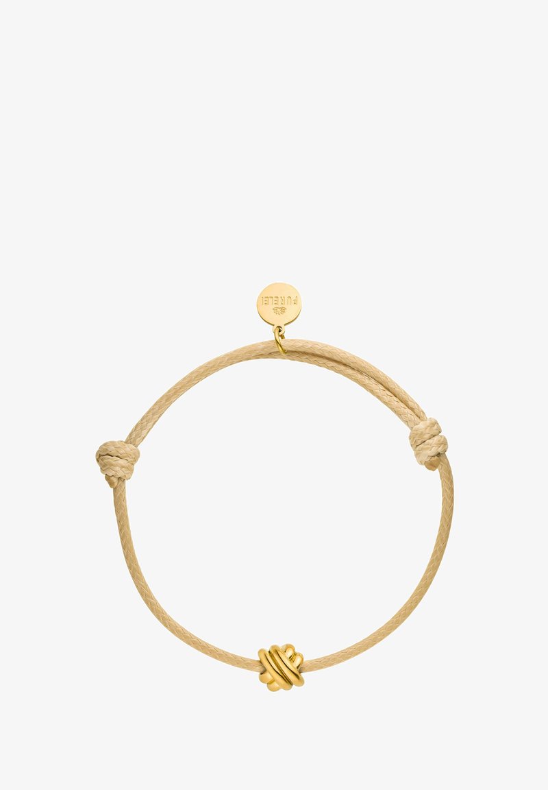 Knot-Armband aus einem beigen geflochtenen Band, verziert mit einem Knoten aus goldfarbenem Metall und einem runden Anhänger. Sanfte Textur mit minimalistischer Gestaltung.