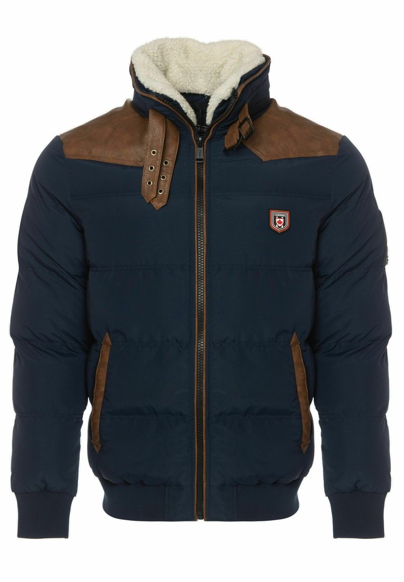 Giacca puffer blu navy con accenti in pelle marrone sulle spalle, colletto foderato in pelliccia, chiusura con zip frontale e tasche laterali. Presenta polsini e orlo a coste.