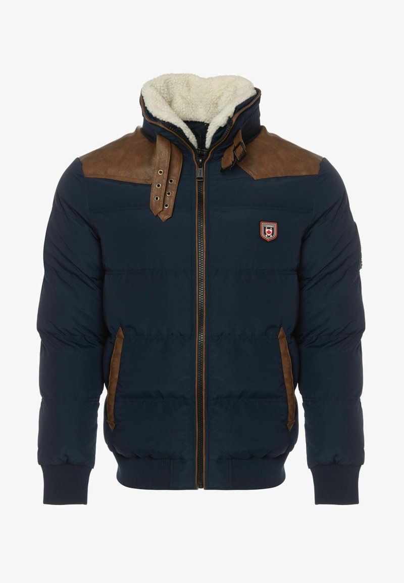 Giacca puffer blu navy con accenti in pelle marrone sulle spalle, colletto foderato in pelliccia, chiusura con zip frontale e tasche laterali. Presenta polsini e orlo a coste.