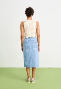Häkelgestricktes, elfenbeinfarbenes Top mit einem strukturierten Muster, kombiniert mit einem hellblauen Denim-Midi-Rock, der zwei Gesäßtaschen und einen Seitenschlitz aufweist.