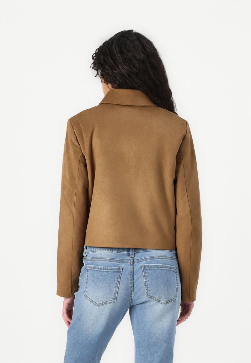 Giacca in faux suede marrone con colletto, design cropped e maniche lunghe, abbinata a jeans in denim azzurro chiaro con tasche posteriori.