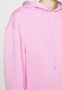 Sudadera con capucha rosa con cordón, confeccionada con tela suave. Presenta un ajuste relajado y un bolsillo tipo canguro, con puños y dobladillo acanalados.