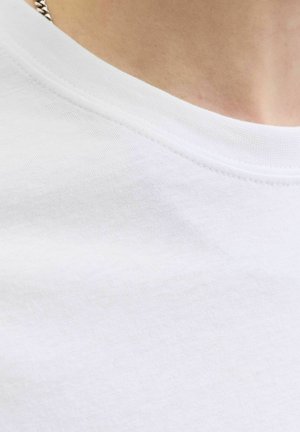 Close-up van een wit shirt met ronde hals, gedragen met een zilveren ketting zichtbaar op de schouder.