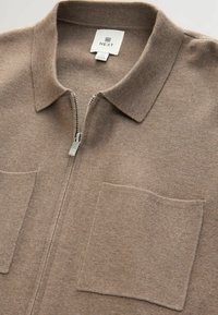 Brun zip-up sweater med krave, lavet af blødt materiale. Har to forlommer og en sølvfarvet lynlås, som viser et minimalistisk design.