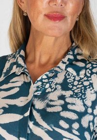 Skjorta i teal med krämfärgad djurtryck, med krage och knappslå. Slät tyg med en lätt glans och strukturerad silhuett.