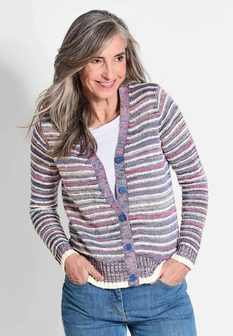 Mehrfarbige Strickjacke mit horizontalen Streifen, blauen Knöpfen und kontrastierenden weißen Rippbündchen und Saum, getragen über einem weißen Oberteil.