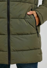 Green padded jacket with a zip closure and side pockets. Features a smooth texture and stitched panels for insulation.