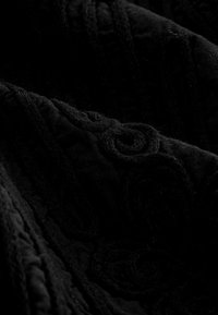 Textil negru cu o textură pufoasă, având modele în spirale și linii nervurate, care creează adâncime și interes vizual.