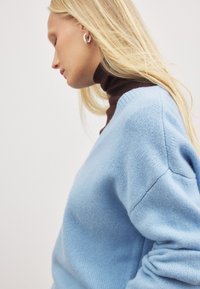 Helles blaues gestricktes Sweatshirt mit lockerer Passform, das über einen tiefen V-Ausschnitt und dezente Rippakzente an den Bündchen und am Ausschnitt verfügt.