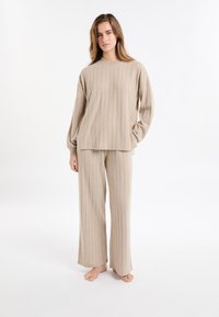 Beżowy sweter z prążkowanego dzianiny i zestaw szerokich spodni. Sweter ma okrągły dekolt; spodnie mają luźny krój. Miękka faktura, casualowy design.