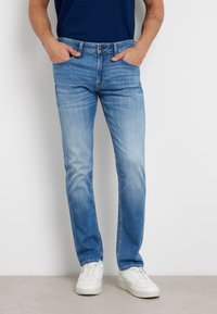 Jasnoniebieskie dżinsy z prostymi nogawkami, z blakniętą fakturą i stylizacją pięciu kieszeni. W połączeniu z białymi trampkami.