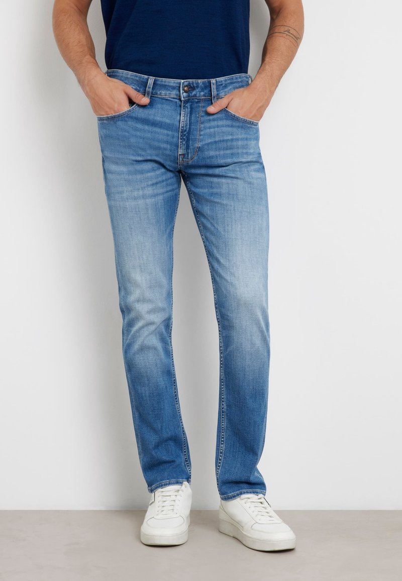 Jasnoniebieskie dżinsy z prostymi nogawkami, z blakniętą fakturą i stylizacją pięciu kieszeni. W połączeniu z białymi trampkami.