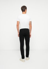 Fekete, skinny farmernadrág sima textúrával, standard derékpánttal és hátsó zsebekkel, egy testre simuló, fehér pólóval és világos lábbelivel párosítva.