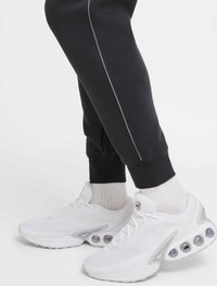 Vita sportskor med en texturerad mesh-ovandel, rund tå och klara bubbel-accenter på sulan. Bärs med svarta avsmalnande joggers och ljusa strumpor.