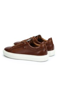 Un paio di sneaker basse in pelle marrone con suole e lacci bianchi, esposti su uno sfondo bianco.