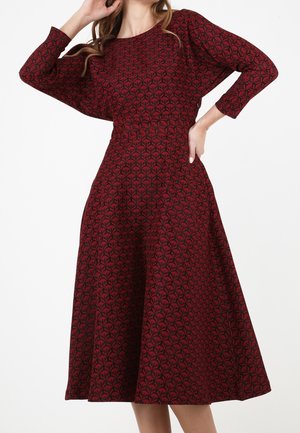 Robe à fleurs rouges avec un col rond, des manches longues et une jupe évasée. Fabriquée en tissu texturé pour un ajustement confortable.