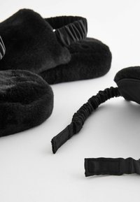 Fionde in pile neri per le orecchie e pantofole, caratterizzate da una consistenza morbida, bande elastiche e un design minimalista. Anche gli accenti sono neri.